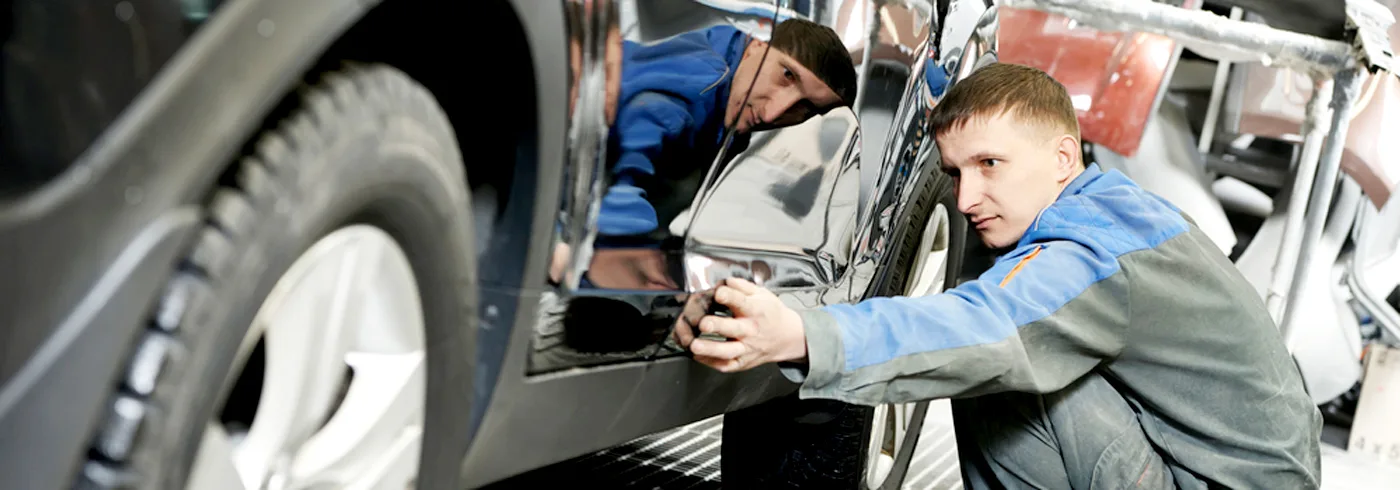 Collision repair technician inspecting and repairing a vehicle body panel