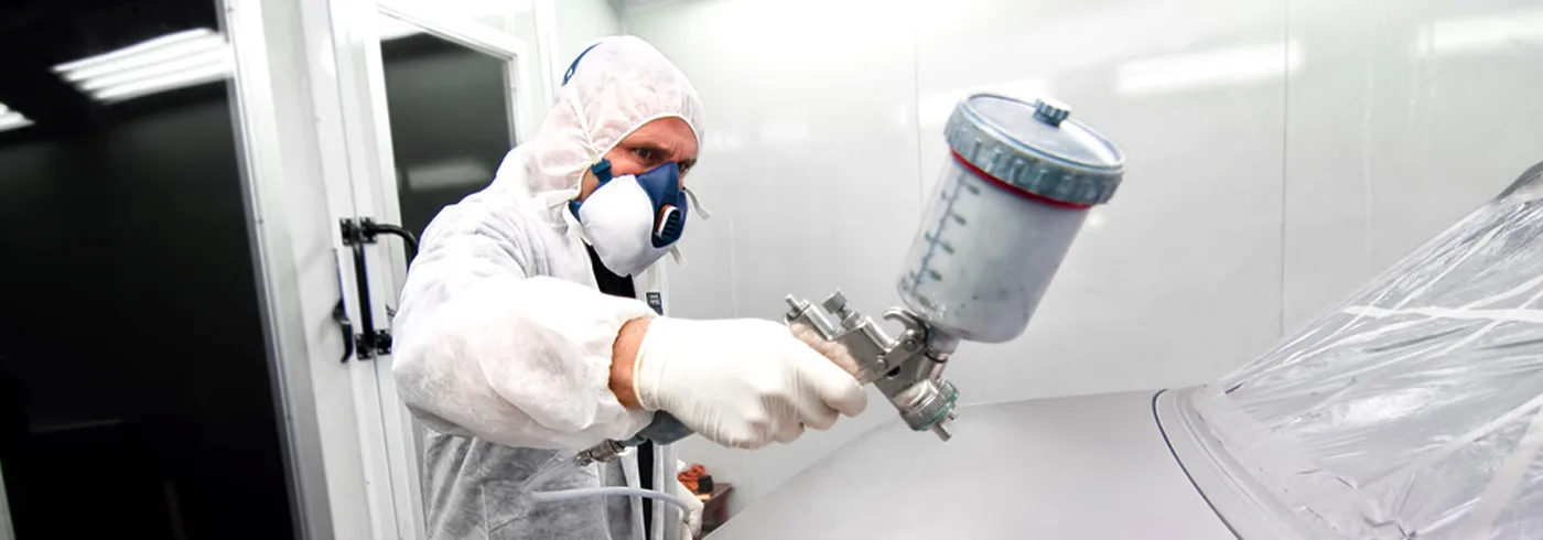 Collision refinishing technician applying paint in a controlled booth